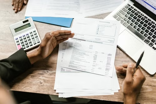 Auditor reviewing financial documents with calculator and laptop